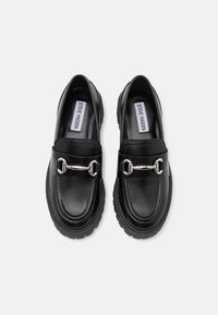 Sorte skinnloafers med en sølvkjede-detalj over vampsen, med en teksturert såle og glatt overflate.