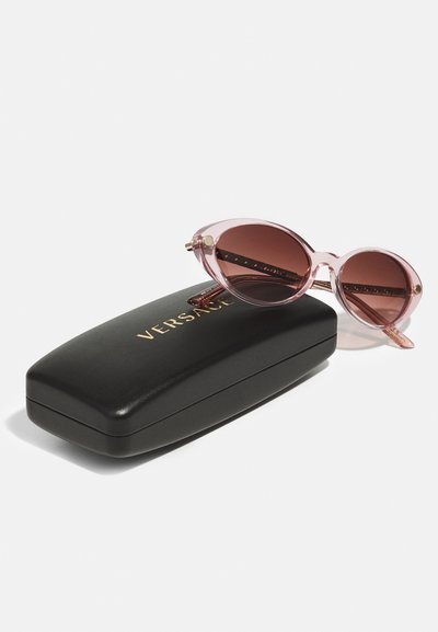 Versace sunglasses with pink translucent frames and brown lenses, placed beside a black hard case embossed with gold lettering.