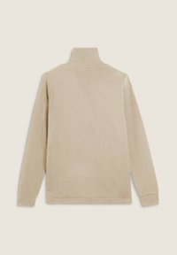 Top beige a maniche lunghe e collo alto realizzato in tessuto morbido. Presenta una superficie liscia e cuciture minime con una vestibilità ampia.