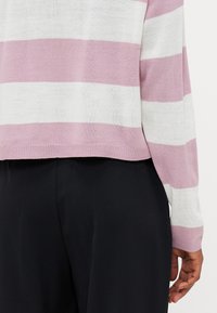 Gestreifter Pullover in Hellrosa und Weiß, mit weicher Strickstruktur, verkürzt geschnitten und mit geripptem Saum. Getragen mit schwarzen Hosen.