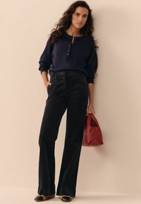 Navy knit sweater with button details, black wide-leg corduroy pants, and a red structured handbag. Shoes are two-tone with a low heel.
