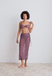 Conjunto de bikini con un top estampado que presenta lazos y una falda larga y ligera a juego. Los colores incluyen burdeos y crema. Textura suave.