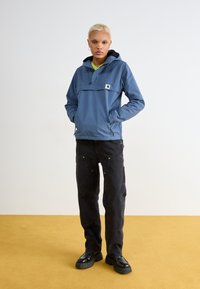 Felpa con cappuccio blu, dotata di tasca frontale e cordini regolabili, abbinata a pantaloni cargo neri con dettagli dorati e robuste scarpe nere.