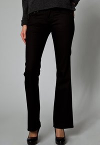 Mustat kellotetut farkut, jotka on valmistettu denimistä, etutaskuilla, napilla ja vetoketjulla suljettavat, sileäpintaiset, yhdistettynä mustiin korkokenkiin.