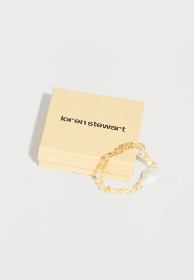 Βραχιόλι με χάντρες και μεγάλη πέρλα δίπλα σε μια μπεζ κουτί κοσμημάτων με την επωνυμία Loren Stewart σε λευκό φόντο.