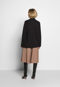 Svart oversize-tröja med långa ärmar, i kombination med beige vida byxor och svarta klackstövlar, sedd bakifrån.