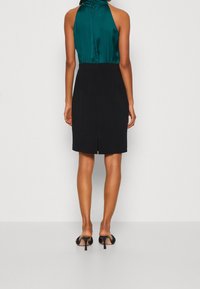 Čern é šaty ke kolenům s saténovým tyrkysovým halter topem, se shromážděným výstřihem a jemným rozparkem na zadní straně, doplněné černými podpatky.