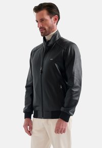 Svart läderbomberjacka med hög krage, framzipper och sidofickor; har ribbade ärmslut och nederkant för en figurnära look.