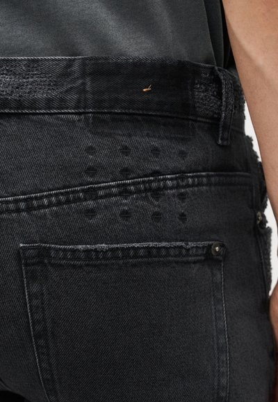 Κοντινό πλάνο μαύρου τζιν με μια μικρή χρυσή παραμάνα προσαρτημένη κοντά στη μέση και μια ορατή πίσω τσέπη.