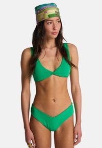 Πράσινο μπικίνι με τριγωνικό τοπ με πιέτες και σλιπ ψηλόμεσο. Το μοντέλο φοράει μαντίλι με σχέδιο στο κεφάλι.