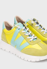 Zapatillas de cuero verde lima y amarillas con detalles en azul claro, presentan cordones blancos, materiales texturizados y una suela blanca gruesa.