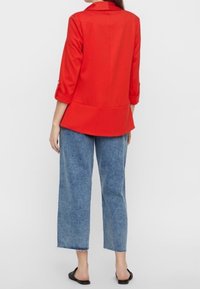 Punainen, kolme neljänneksen hihoilla varustettu bleiseri, jossa on jämäkkä istuvuus, yhdistetty vaaleansinisiin leveälahkeisiin farkkuihin ja mustiin liukusandaaleihin.