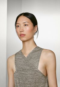 Ärmelloses Top mit V-Ausschnitt aus einem strukturierten grauen Stoff. Verfügt über ausgeschnittene Seiten und einen lässigen Schnitt, der das minimalistische Design ohne Verzierungen betont.