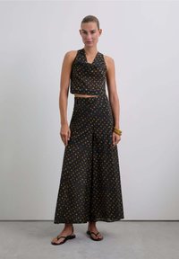 Conjunto de top halter negro y pantalones de pierna ancha con un patrón geométrico multicolor; tejido ligero, corte relajado, combinado con sandalias negras.