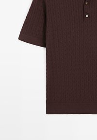 Bruin gebreid poloshirt met korte mouwen, kabelpatroon, geribbelde manchetten en een twee knopen tellende knoopsluiting, afgebeeld op een witte achtergrond.