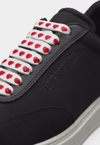 Μαύρο sneaker Moschino με λευκά κορδόνια διακοσμημένα με κόκκινες καρδιές και λευκή σόλα.