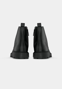 Paire de bottines en cuir noir avec semelles épaisses et fermetures éclair arrière, vues de dos sur un fond clair uni.
