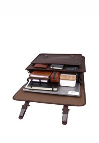 Serviette en cuir marron ouverte avec compartiments organisés contenant un ordinateur portable de 15 pouces, des cahiers, un téléphone, un portefeuille, une pochette et un petit récipient.