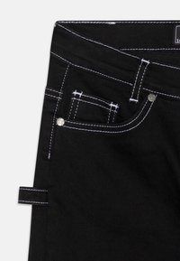 Czarne dżinsy z kontrastującym białym przeszyciem, pięciokieszeniowym wzorem oraz metalowymi ozdobami. Wyposażone w pętlę do przyczepienia paska.