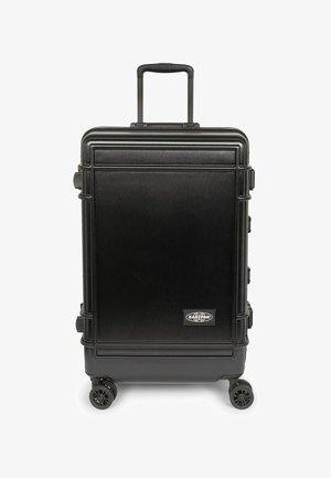 Valise rigide noire à texture brossée, poignée extensible, quatre roues et plaque logo, avec une forme rectangulaire et des bords doublés.