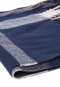 Coperta in lana, blu scuro con motivo grigio chiaro e bianco, texture morbida, piegata con cuciture e dettagli dei bordi visibili.