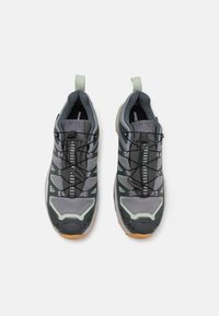 Buty sportowe z szaro-siatkowym cholewką z zielonymi akcentami, teksturowaną podeszwą, elastycznymi sznurówkami i uchwytami do łatwego zakładania.