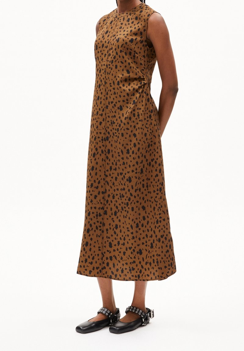 Robe midi marron sans manches avec des taches noires irrégulières, portée avec des chaussures plates noires à brides à œillets et boucles.