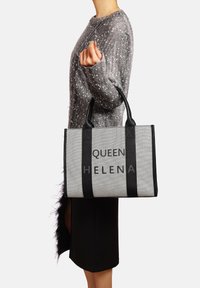 Borsa tote in tessuto grigio con manici neri; presenta la scritta "QUEEN HELENA" stampata in lettere grasse. La borsa ha una forma e una texture strutturate.