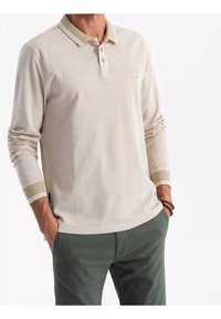 Polo à manches longues beige avec une finition texturée, patte de boutonnage à deux boutons, et rayures contrastantes sur le col et les poignets. Logo discret sur la poitrine.