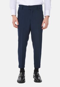 Pantaloni sartoriali blu navy con una texture liscia, dotati di chiusura a bottone, passanti per cintura e orli arrotolati, abbinati a mocassini neri e calzini.
