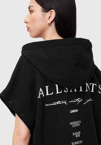 Melnas kapuces pončo ar īsām piedurknēm, uz muguras ir balts "ALLSAINTS" logotips un teksta detaļas. Mīksts audums un pogu akcenti.