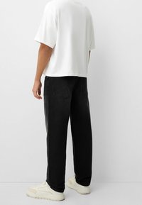 Camiseta blanca de manga corta combinada con jeans anchos negros y zapatillas color crema. Los jeans presentan un diseño clásico de cinco bolsillos.