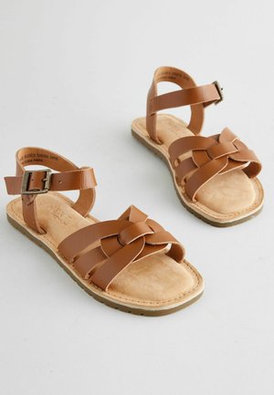 Hnedé kožené sandále s tkanými popruhmi, plochou podrážkou a nastaviteľnou prackou. Stielka je polstrovaná a má textúrovaný povrch.