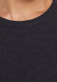 Suéter gris carbón, tejido texturizado con acabado de canalé, cuello redondo y mangas cortas. La vista en primer plano destaca los detalles del material.