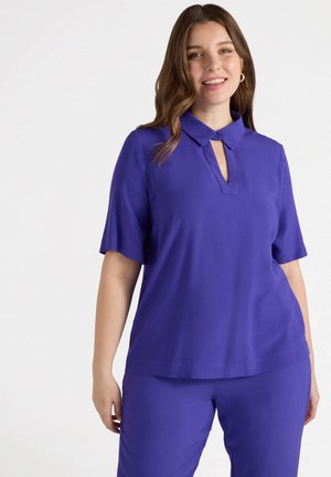Blusa viola a maniche corte con colletto a camicia e dettaglio a chiave sul collo. Tessuto liscio e leggero. Abbinata a pantaloni coordinati.