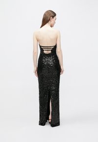 Juoda vakarinė suknelė su blizgančiomis kalnų krištolo detalėmis, aptempta silueto, su išpjova nugaroje ir trimis plonomis petnešėlėmis. Vienoje pusėje yra didelė šlaunies pjūvimo sklendė.