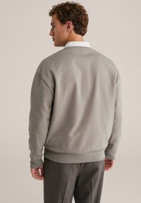 Šedá mikina s okrúhlym výstrihom vyrobená z mäkkej bavlnenej zmesi, s rebrovanými manžetami a lemom, nosená cez kárované nohavice. Pohľad zozadu odhaľuje minimálne detaily.