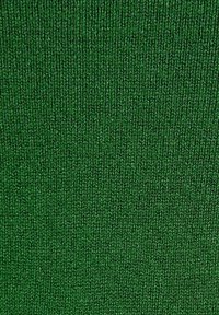 Gros plan sur un tissu vert tricoté avec une texture côtelée verticale et des points de fil visibles.