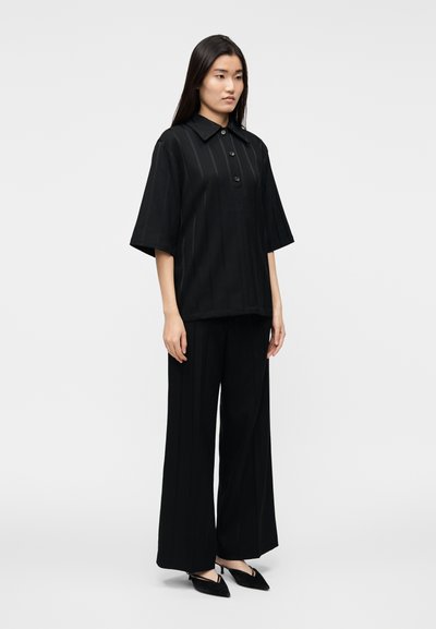 Completo in tessuto nero composto da una maglia a maniche corte con colletto e bottoni e pantaloni a gamba larga, entrambi con righe verticali e una texture liscia.