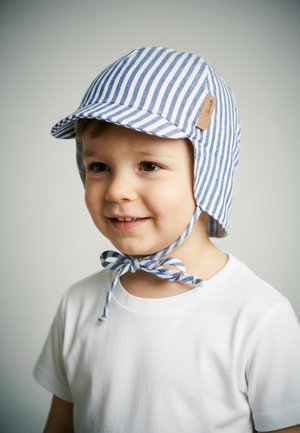 Junges Kind trägt einen blau-weiß gestreiften Sonnenhut, der unter dem Kinn gebunden ist, und ein schlichtes weißes T-Shirt, lächelt und schaut leicht nach rechts.