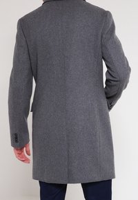 Abrigo de lana gris con corte recto, abertura trasera única y mangas largas. Presenta puños abotonados y un diseño limpio y minimalista.