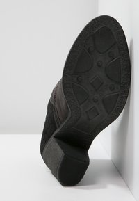 Scarpa in camoscio nero con suola testurizzata e tacco basso, che mostra un motivo spesso e una superficie piatta per la presa, vista da un angolo laterale.