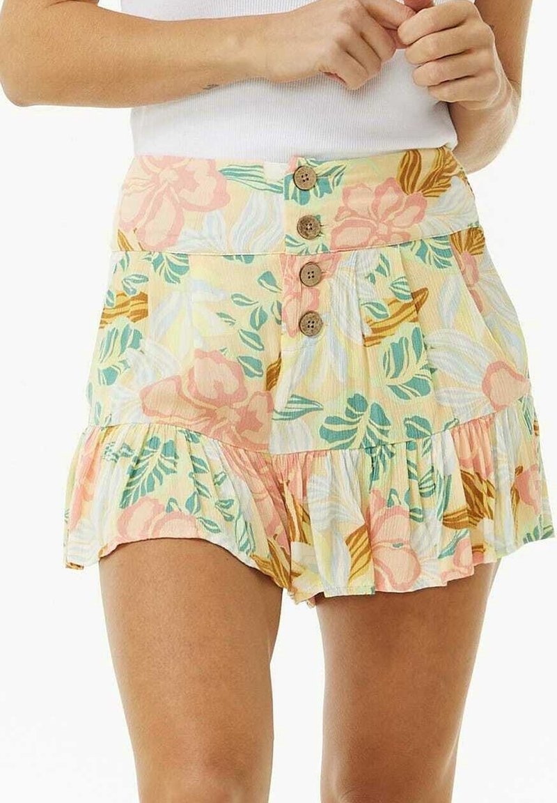 Shorts à motif floral avec quatre boutons en bois à l'avant et ourlet à volants, portés avec un haut blanc sans manches.