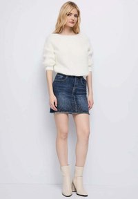 Maglione bianco e soffice lavorato a maglia con spalle scese, abbinato a una minigonna in denim scuro con orlo sfrangiato. Stivaletti beige con zip.