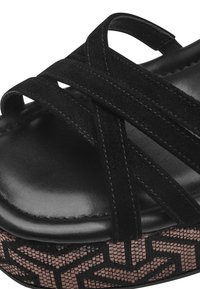 Sandal peep toe nera con cinturini incrociati in camoscio e parte superiore lucida simile alla pelle. Il tacco a cuneo è impreziosito da una base a motivo geometrico.