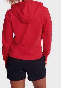 Rode hoodie met lange mouwen en een relaxte pasvorm, gecombineerd met zwarte shorts, die een soepele stofstructuur laten zien.