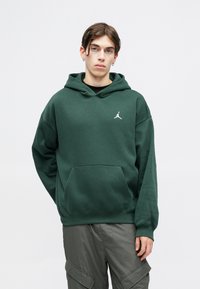 Fleece verde com um bolso canguru, apresentando o logótipo branco da Jordan. Feita de um material suave, tem um corte confortável e capuz ajustável com cordão.