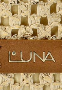 Tejido beige tejido con un patrón texturizado, que presenta una etiqueta de cuero marrón con la palabra "LUNA" grabada en letras plateadas.