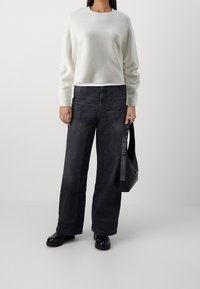 Valkoinen neule, mustat leveälahkeiset farkut näkyvällä ompeleella ja mustat nilkkurit. Musta laukku säädettävällä hihnalla.