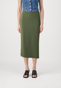 Grønn, knelangs skjørt laget av elastisk stoff med strikk i midjen. Brukt med åpne, svarte sandaler.